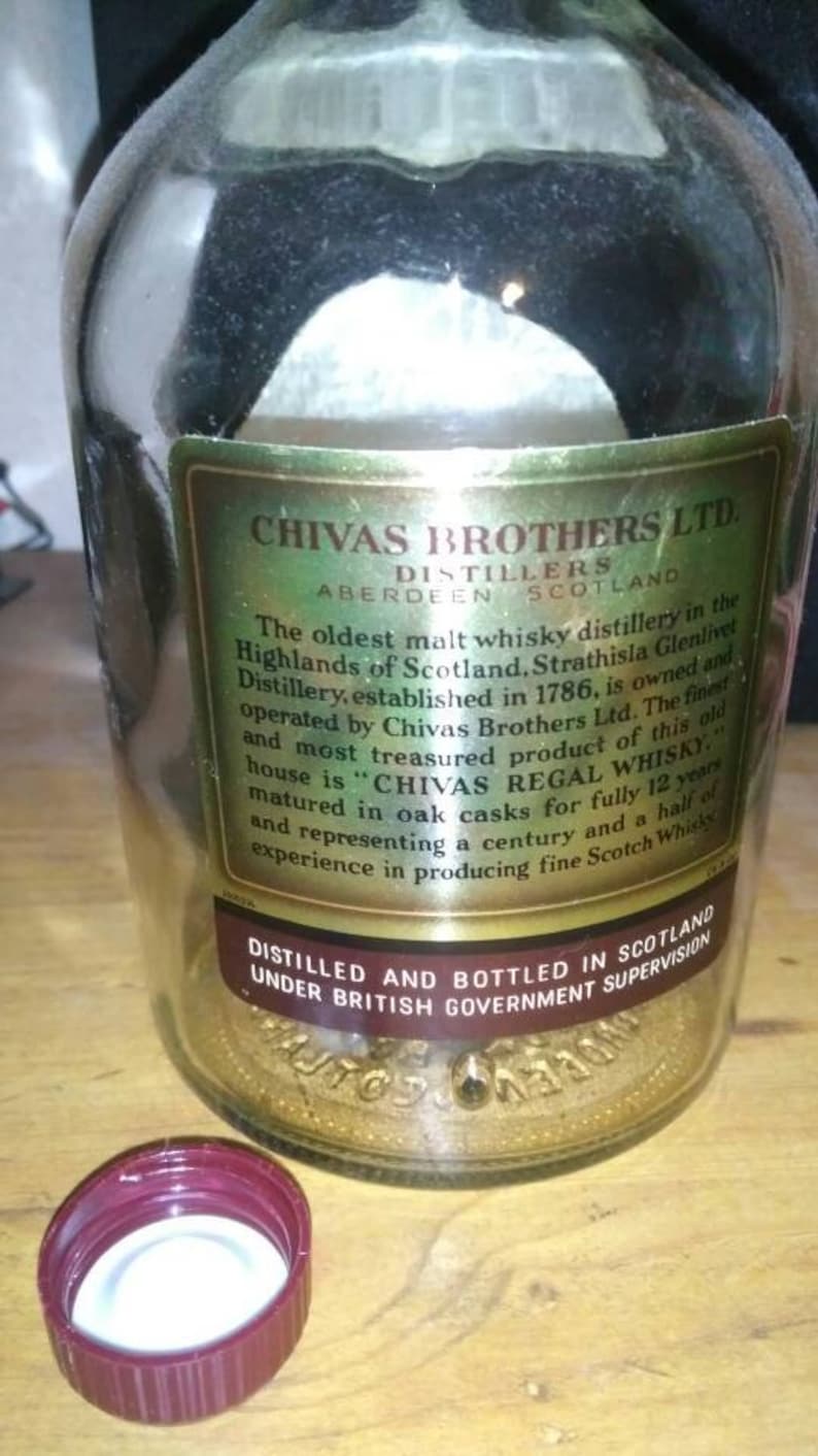 Op de afbeelding: Een close-up van een etiket van een Chivas Brothers Ltd. Scotch whisky-fles. Het etiket is goudkleurig met zwarte tekst en vermeldt dat de distilleerderij de oudste malt whisky-distilleerderij in de Schotse Hooglanden is. Het etiket vermeldt ook dat de distilleerderij in 1786 werd opgericht en eigendom is van en wordt ge&euml;xploiteerd door Chivas Brothers Ltd. Het etiket vermeldt ook dat het beste en meest gewaardeerde product van dit oude huis "Chivas Regal Whisky" is en dat het 12 jaar lang in eiken vaten wordt gerijpt.