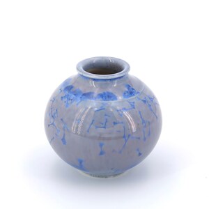 Puede incluir: Un pequeño jarrón redondo de cerámica azul y blanco con un esmalte craquelado.