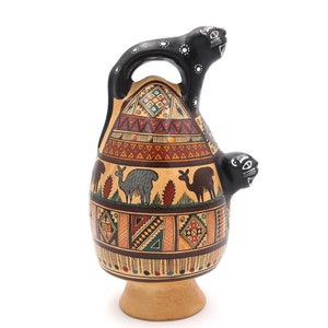 May include: A ceramic jug with a black handle and two black animal heads on the sides. The jug is decorated with geometric patterns and images of llamas in brown, red, and blue.