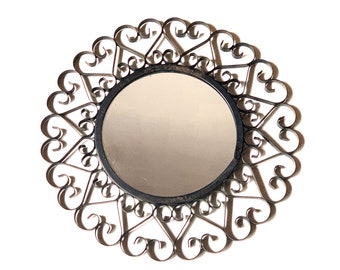 Puede incluir: Un espejo redondo con un marco de metal decorativo hecho de formas de corazón en espiral. El marco es de color plateado.