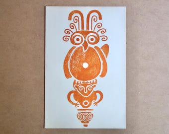 May include: Orange print on a light blue background. The print features a stylized owl figure atop a human-like figure, with a vase at the bottom. The owl has large eyes and decorative head feathers. The figures are in a stacked arrangement.