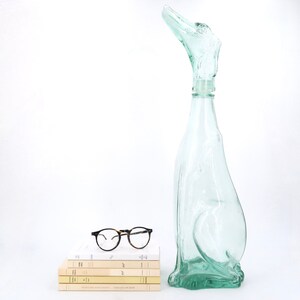 Peut inclure: Une bouteille en verre vert clair avec un design abstrait unique. &Agrave; c&ocirc;t&eacute;, une pile de livres et des lunettes rondes &agrave; monture noire. Le design de la bouteille ressemble &agrave; un oiseau ou un animal.