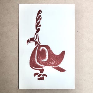May include: A maroon-colored illustration of a stylized bird with a large crest and a curved beak. The bird is standing on a small pedestal, and the artwork is printed on a white rectangular card.