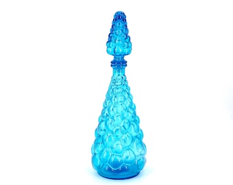 May include: A blue glass bottle with a textured, bubble-like design. The bottle has a tall, narrow neck and a pointed top.