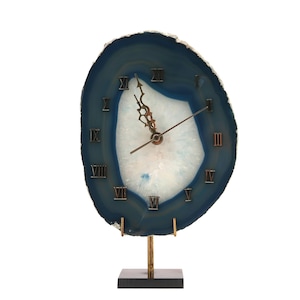May include: A decorative clock made from a blue and white agate slice. The clock face features Roman numerals and bronze-colored hands. It is mounted on a bronze stand with a black base.