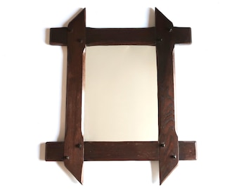 May include: A dark brown wooden mirror with a rectangular shape. The frame has a unique design with angled top and bottom pieces, and is held together with small, dark-colored pegs. The mirror's surface is a light beige color.