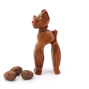 May include: A wooden nutcracker shaped like a dog. The dog is brown and has a red tongue. The nutcracker is standing on a white surface with three walnuts in front of it.