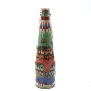 Peut inclure: Une bouteille décorative en verre avec un bouchon en liège, remplie de couches de sable coloré. L'art du sable représente un paysage avec des bâtiments, des arbres et des motifs géométriques dans des tons de vert, rouge, orange, bleu et blanc. La bouteille mesure environ 25 cm de haut.