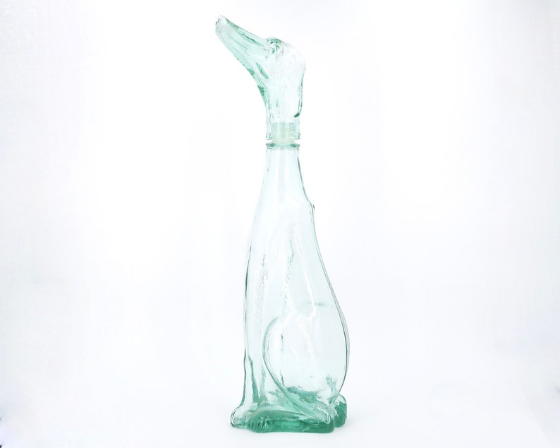 Peut inclure: Une bouteille en verre transparent en forme de chien, avec la t&ecirc;te du chien formant le bouchon. La bouteille est de couleur vert clair et pr&eacute;sente un design lisse et incurv&eacute;. Le chien est assis.
