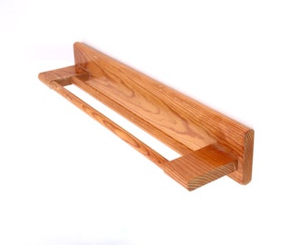 May include: A wooden wall-mounted shelf with a towel bar. The shelf is made of light brown wood and has a natural finish. The towel bar is made of the same wood and is attached to the shelf with two metal brackets.