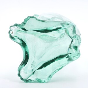 Peut inclure: Un objet en verre transparent vert clair de forme organique unique. Le verre pr&eacute;sente une texture ondul&eacute;e et un bord festonn&eacute;, cr&eacute;ant une pi&egrave;ce d&eacute;corative et artistique. L'objet est pos&eacute; sur un fond blanc.