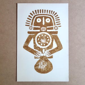 May include: Brown print on white paper of a stylized figure with a headdress, holding a circular object and a sack. The figure has a geometric design and a symmetrical composition. The artwork is a linocut print.