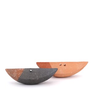 May include: Two ceramic half-moon shaped dishes. One dish is black with a brown rim and the other is brown with a black rim. Both dishes have small holes.