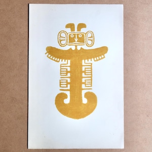 May include: A print featuring a stylized, golden-yellow figure on a white background. The figure has a head with large ears, a rectangular body, and outstretched arms. The design has a tribal or ancient art aesthetic.