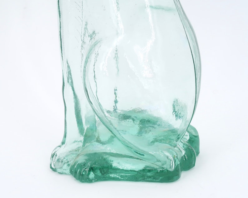 Peut inclure: Une figurine de chat en verre transparent vert clair. Le chat est assis, avec ses pattes avant visibles. Le verre a une surface l&eacute;g&egrave;rement textur&eacute;e. La figurine est sur fond blanc.