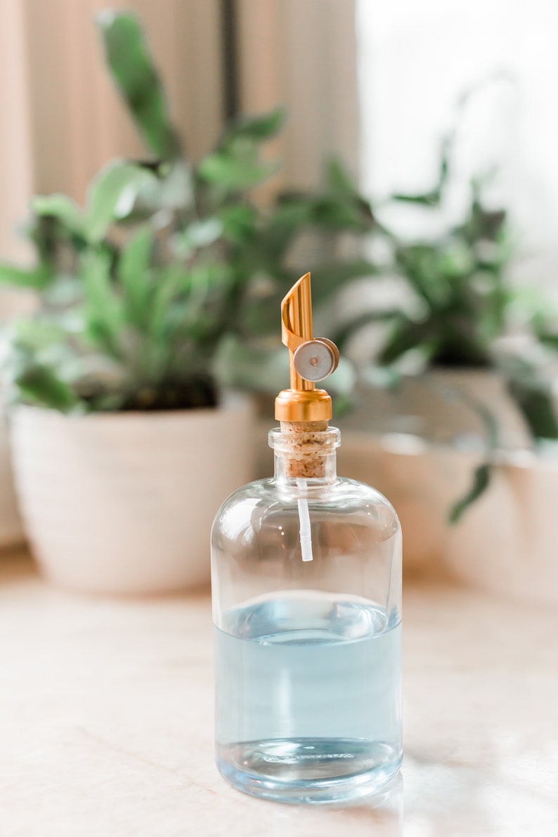 May include: A clear glass bottle with a blue liquid inside and a gold metal pump top. The bottle is sitting on a white surface.