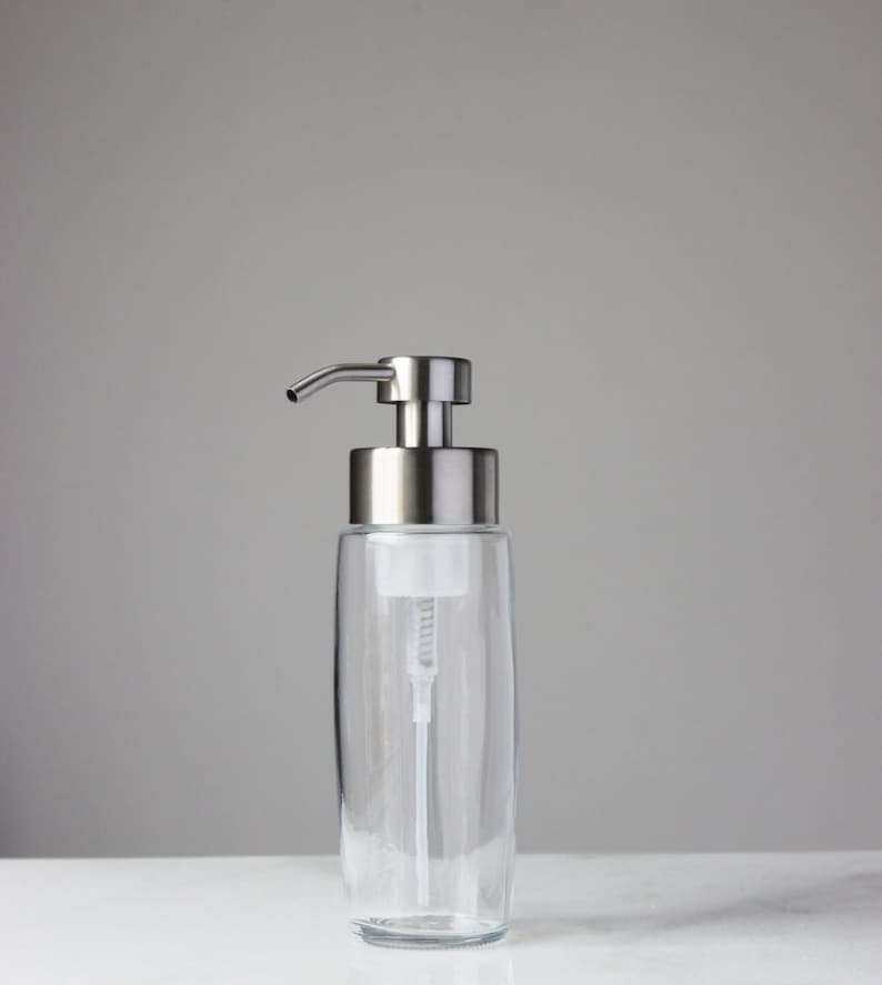 May include: A clear glass soap dispenser with a silver pump. The dispenser has a sleek, modern design and is perfect for any bathroom.