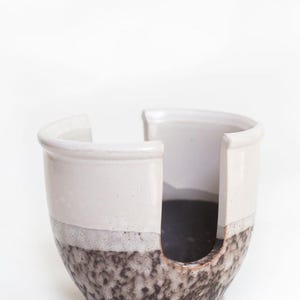 May include: A white ceramic yarn bowl with a brown and white speckled glaze. The bowl has a cut-out for yarn to be dispensed.