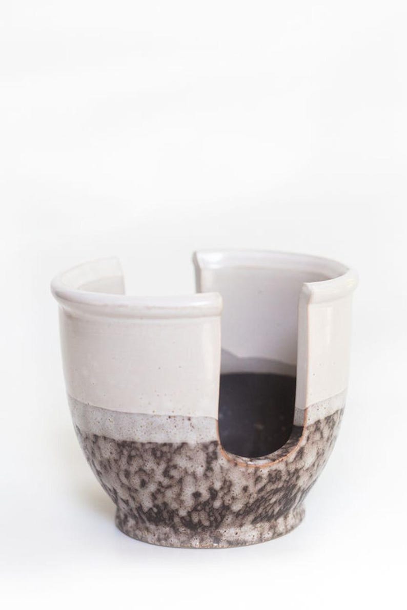 May include: A white ceramic yarn bowl with a brown and white speckled glaze. The bowl has a cut-out for yarn to be dispensed.