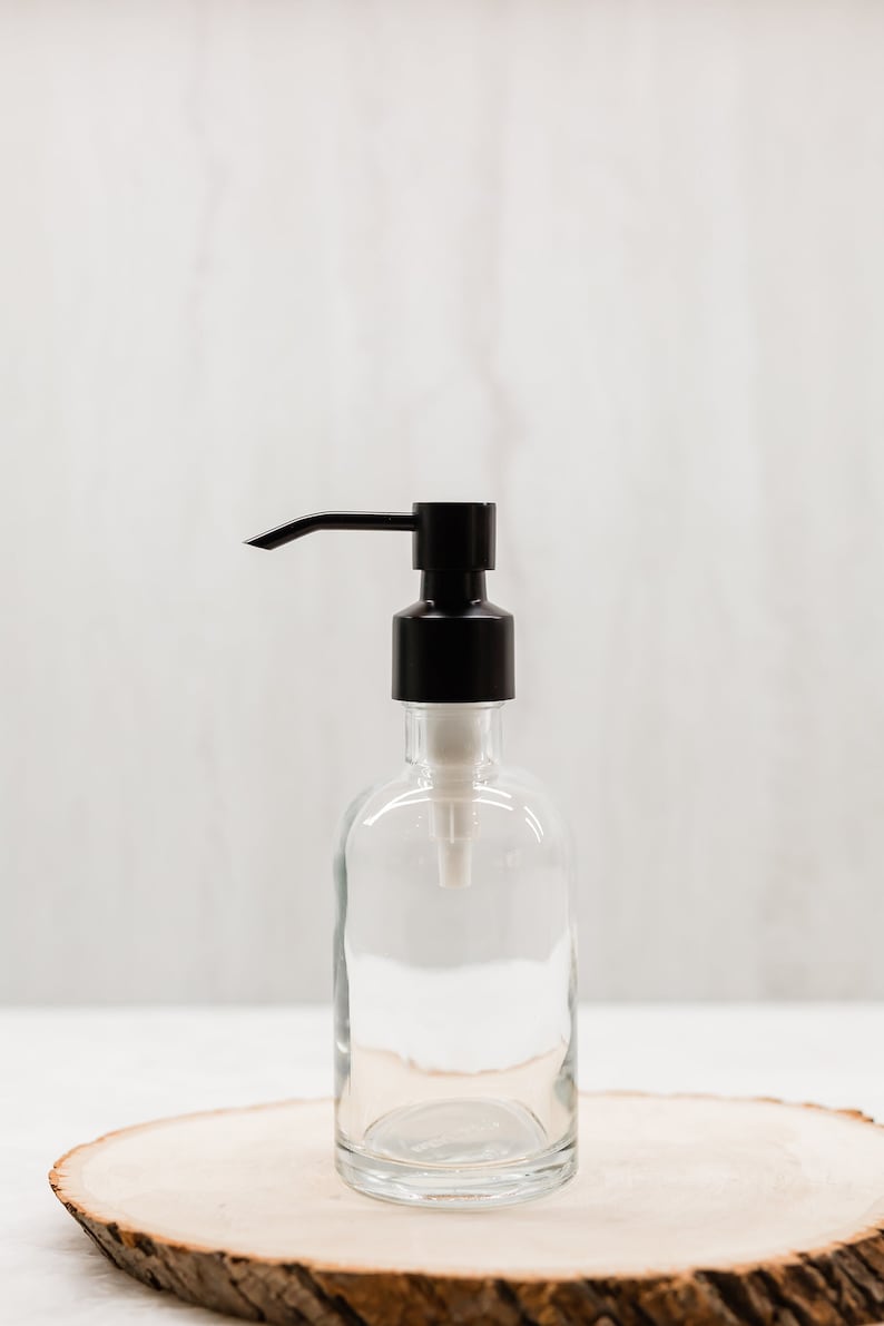May include: A clear glass bottle with a black pump dispenser. The bottle is sitting on a wooden slice.