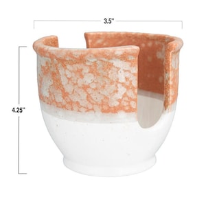 May include: A white ceramic paper towel holder with a speckled orange glaze. The holder measures 3.5 inches wide and 4.25 inches tall.