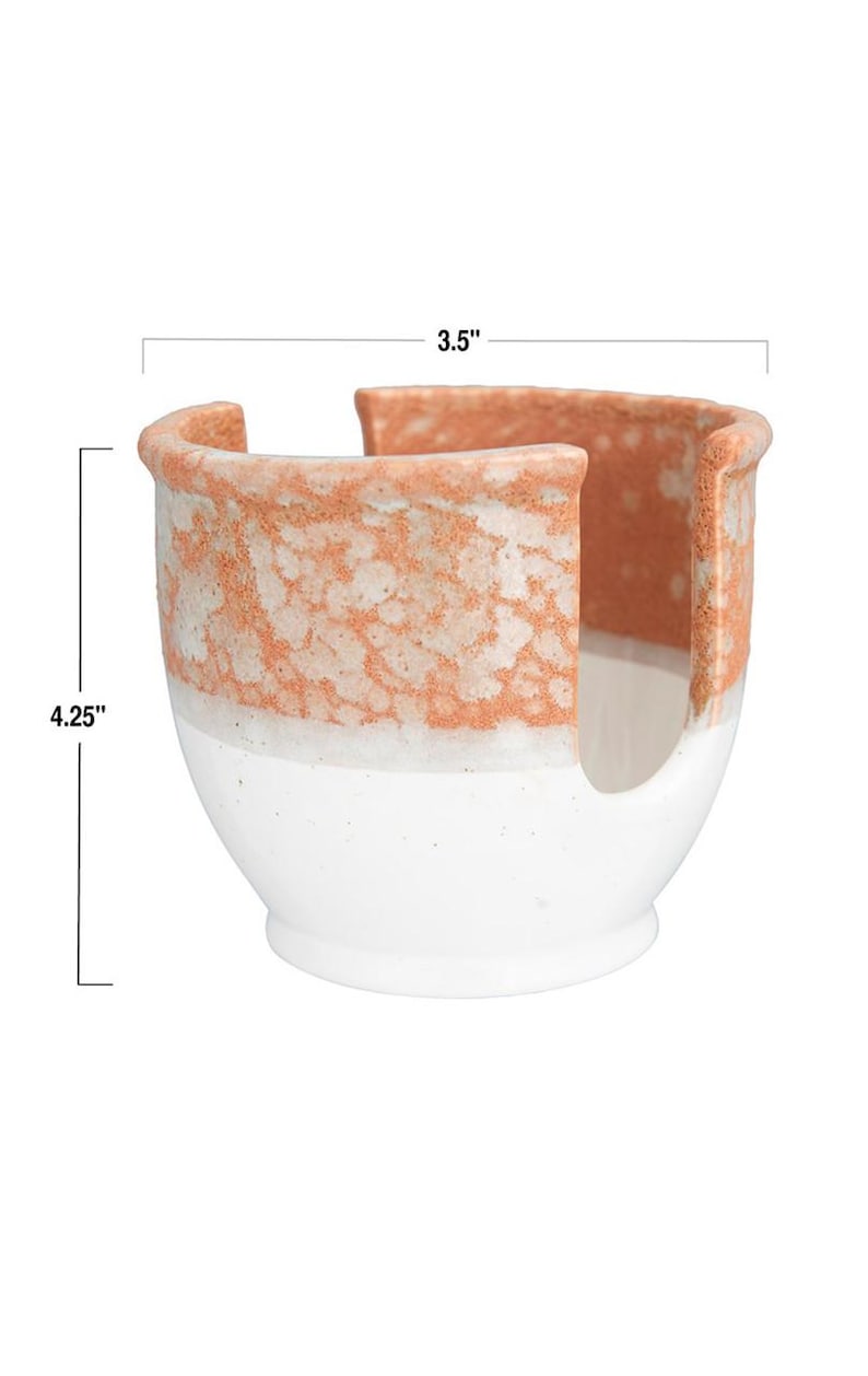 May include: A white ceramic paper towel holder with a speckled orange glaze. The holder measures 3.5 inches wide and 4.25 inches tall.