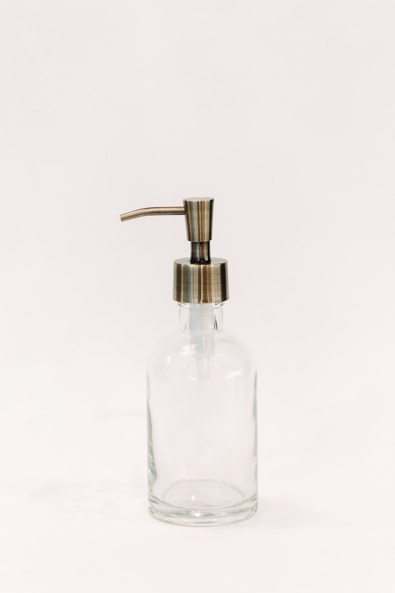 May include: A clear glass soap dispenser with a brushed nickel pump. The dispenser is empty and has a simple design.