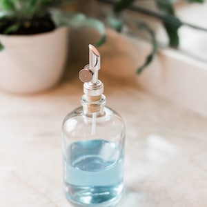 May include: A clear glass bottle with a silver pump dispenser filled with light blue liquid. The bottle is sitting on a white marble surface.