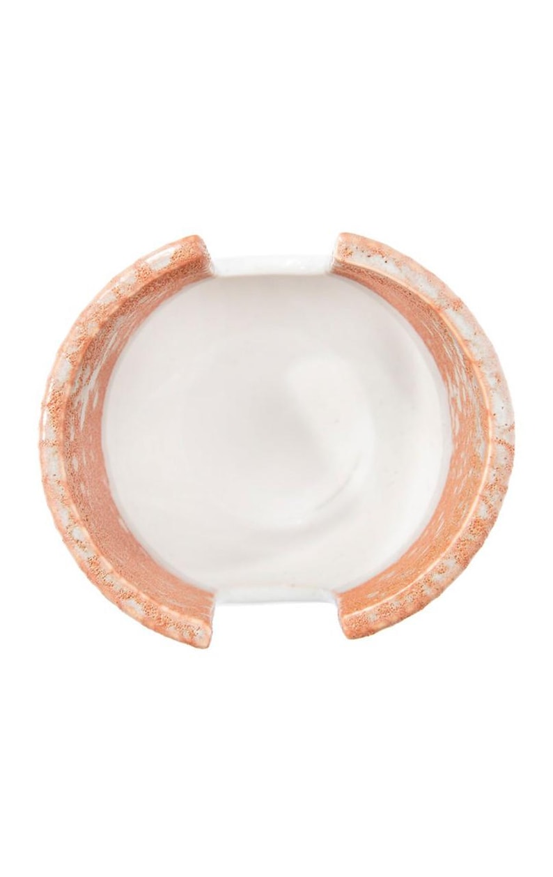 May include: A white ceramic dish with a terracotta rim. The dish has a unique shape with two cutouts on the sides.