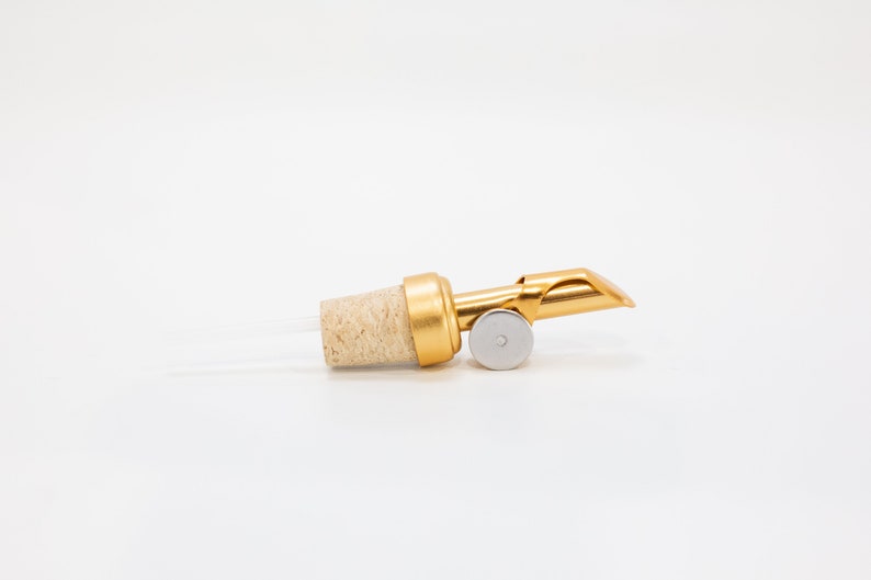 May include: Gold bottle pourer with a cork stopper and a metal spout. The spout is designed to control the flow of liquid.