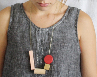 May include: A simple necklace with geometric shapes in pink, red, and gold. The necklace is made of wood and is strung on a thin cord.