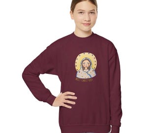May include: A maroon sweatshirt featuring a graphic of a saintly figure with a gold halo and the text "Meet Christ Kids". The illustration is centered on the front of the long-sleeved top.