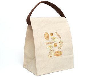 May include: A beige canvas lunch bag with a brown handle. The bag features a watercolor illustration of various types of bread, including baguettes and rolls. The bag is designed to be reusable.