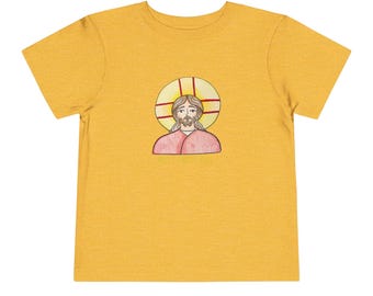 May include: Mustard yellow toddler t-shirt featuring a hand-drawn illustration of a religious figure with a halo. The illustration depicts a figure with a beard and long hair, wearing a red garment. The halo is yellow with red cross-shaped lines.