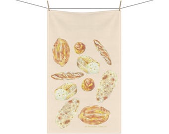 May include: A beige towel featuring watercolor illustrations of various types of bread, including baguettes, loaves, and rolls. The bread is depicted in shades of brown and gold, with detailed textures. The towel is hanging from a clothesline.