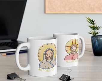 May include: Two white ceramic mugs with illustrations of religious figures. One mug features a woman with a halo, the other depicts a man with a halo. Both mugs have the text "MEET CHRIST KIDS" in yellow.