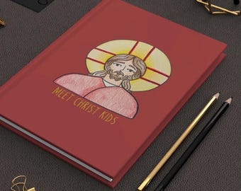May include: A red journal with the text "MEET CHRIST KIDS" and an illustration of Jesus. The journal is accompanied by gold and black pencils and gold binder clips. The cover art features a drawing of Jesus with a halo.