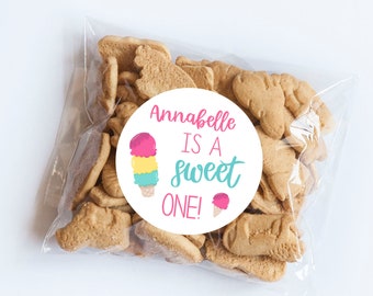May include: A transparent bag containing light brown biscuits in various shapes. A circular sticker on the bag says "Annabelle IS A sweet ONE!" with an ice cream cone illustration in pink, yellow, and blue.