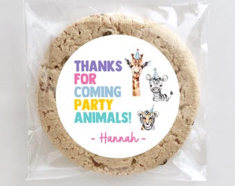 May include: A chocolate chip cookie in a clear cellophane bag. The cookie has a white circular sticker with the text "THANKS FOR COMING PARTY ANIMALS!" and illustrations of a giraffe, zebra, and tiger, all wearing party hats. The name "Hannah" is also on the sticker.