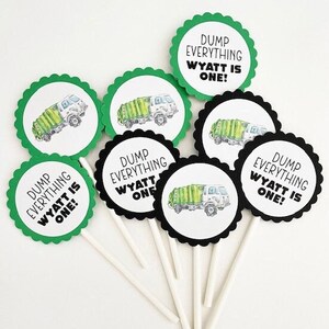 May include: Green and black cupcake toppers with a garbage truck design and the text "Dump Everything Wyatt is One!"