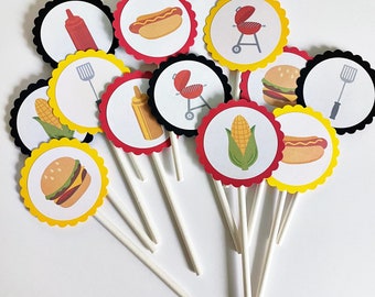 Puede incluir: Un conjunto de 10 adornos para cupcakes con varias ilustraciones de temática barbacoa, incluyendo perritos calientes, mazorcas de maíz, hamburguesas, herramientas para asar y una parrilla. Los adornos están impresos en cartulina blanca con acentos rojos, amarillos y negros y tienen bordes festoneados.