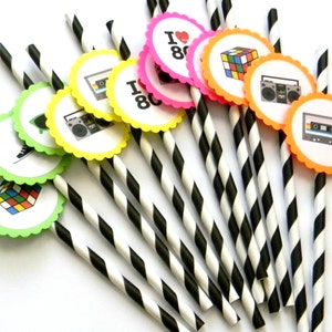 May include: A set of black and white striped paper straws with colorful round paper toppers featuring 80s icons like a cassette tape, boombox, Rubik's Cube, and the text "I love the 80s".