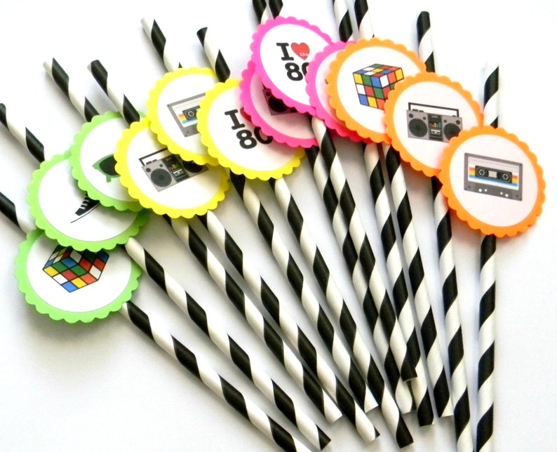 May include: A set of black and white striped paper straws with colorful round paper toppers featuring 80s icons like a cassette tape, boombox, Rubik's Cube, and the text "I love the 80s".