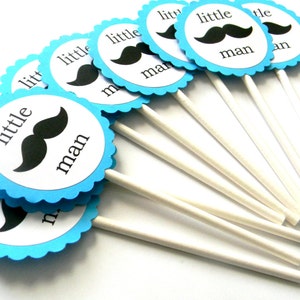 May include: A set of blue and white cupcake toppers with a black mustache and the text "little man".