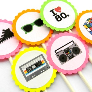 May include: Six colorful cupcake toppers with 80s themed designs. The toppers feature a cassette tape, a boombox, a pair of sunglasses, a Rubik's Cube, a high-top sneaker, and a heart with the text "I love the 80s".