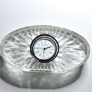 May include: A clear crystal oval clock base with a silver face clock that reads "Waterford".