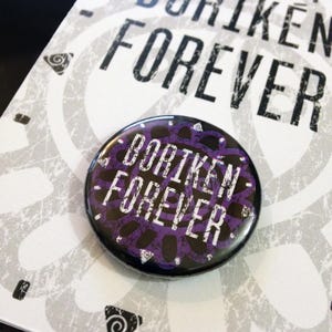 May include: A black and purple button with the text "BORIKEN FOREVER" in white lettering. The button has a circular design with a purple center and black outer ring.