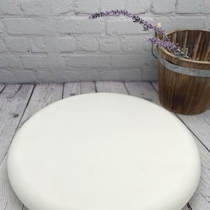 May include: White round cake stand with a smooth, slightly domed surface. The stand is made of a sturdy material and is perfect for displaying cakes, cupcakes, or other desserts.