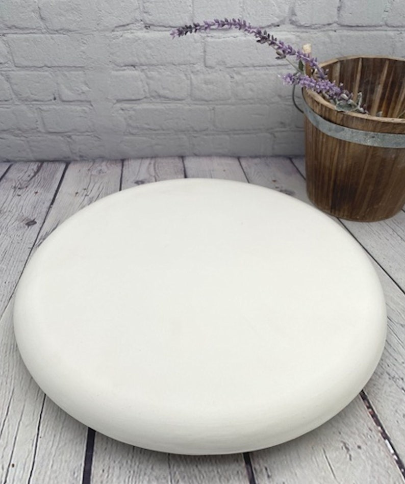 May include: A white round cake stand with a smooth, slightly rounded surface. The stand is made of a sturdy material and is perfect for displaying cakes, cupcakes, or other desserts.