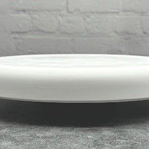 May include: A white, round, ceramic plate with a slightly raised edge. The plate has a matte finish and appears to be new. The plate is suitable for serving food or as a decorative item.